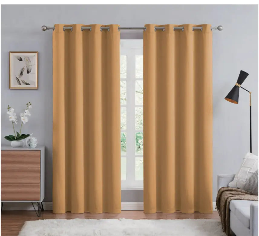 Mustard yellow curtains hanging in a room with a lamp, plant, and wall art.