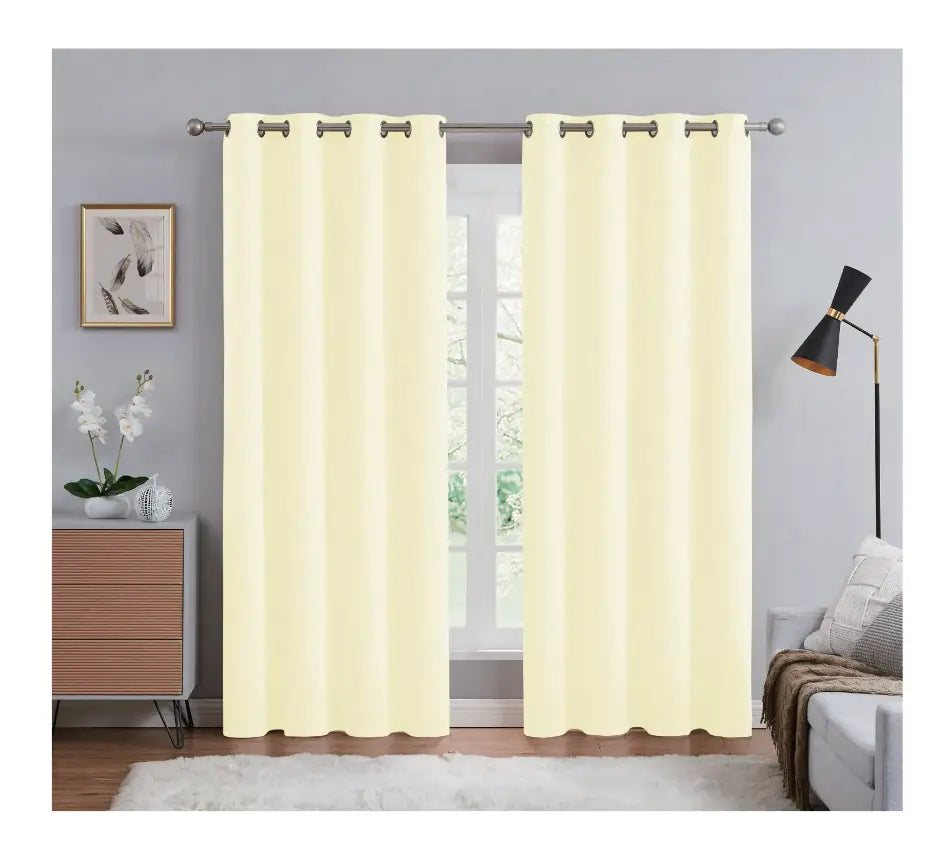 Pair of yellow curtains hanging in a room with a window, side table, and lamp.