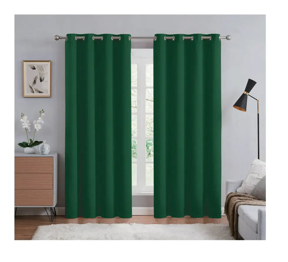 Green curtains hanging in a room with a lamp, plant, and furniture.