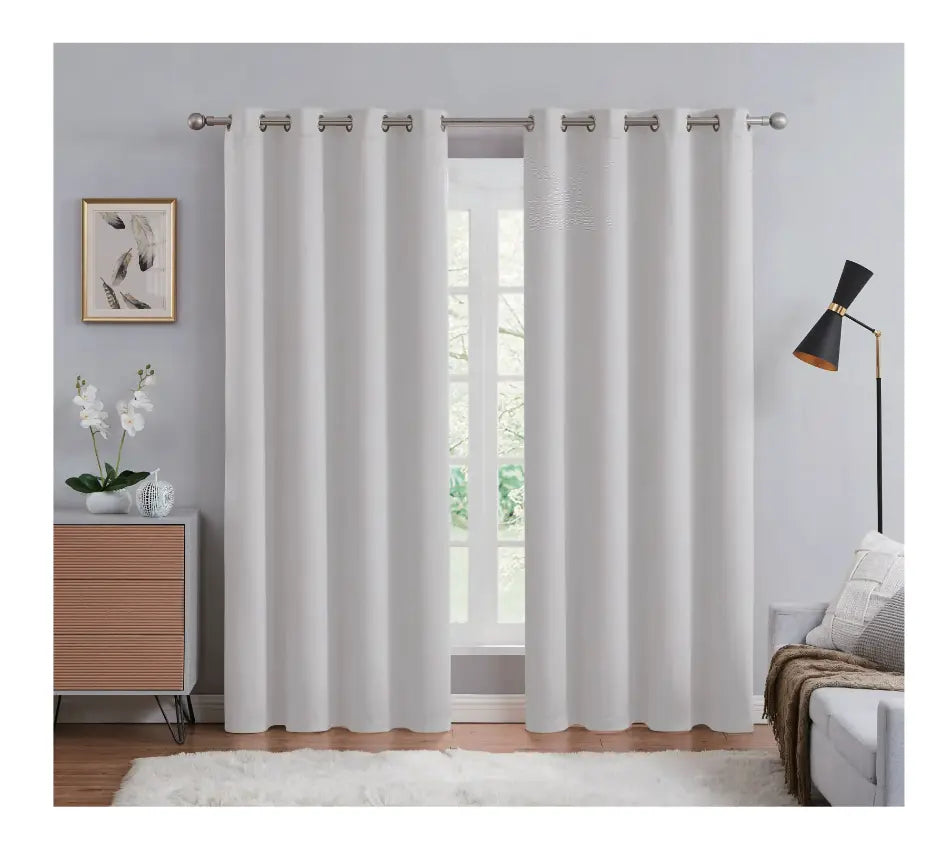 White curtains hanging in a room with a window, light gray walls, a wooden side table, and a lamp.