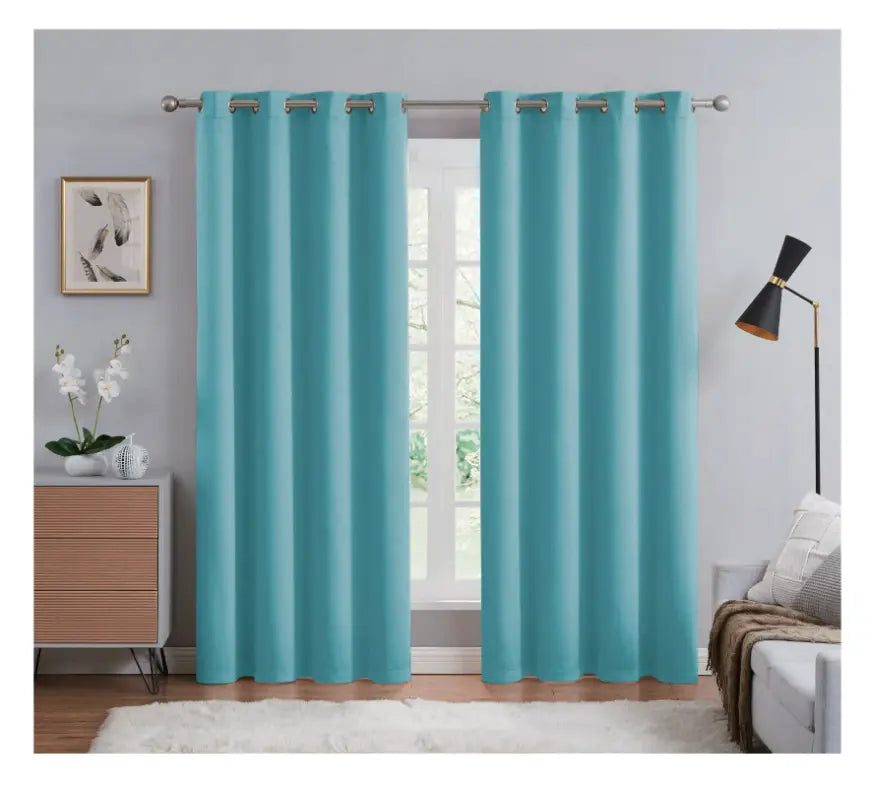 Teal curtains hanging in a room with a bed, lamp, and dresser.