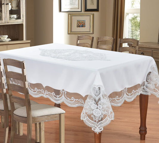 A white rectangular tablecloth with an embroidered floral motif in the center and scalloped lace trim along the edges, shown draped over a wooden dining table in a furnished dining room.