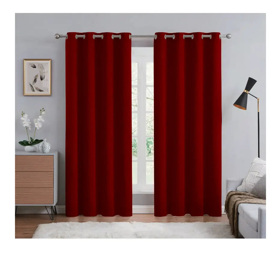 Red curtains hanging in a room with a window, lamp, and decor items.