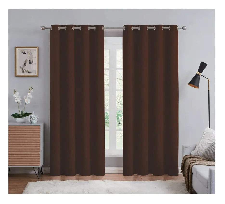Brown curtains hanging in a room with a bed, lamp, and decor items.