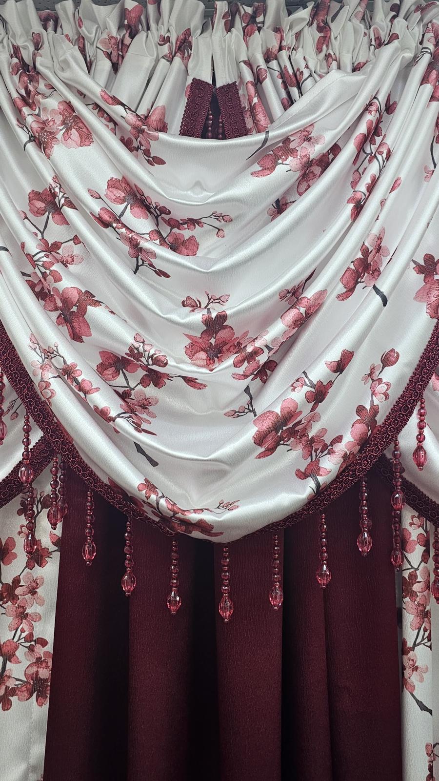 A close-up of a draped curtain or valance with a white satin-like upper panel printed with pink cherry blossom flowers and dark burgundy trim, layered over a deep burgundy curtain panel.