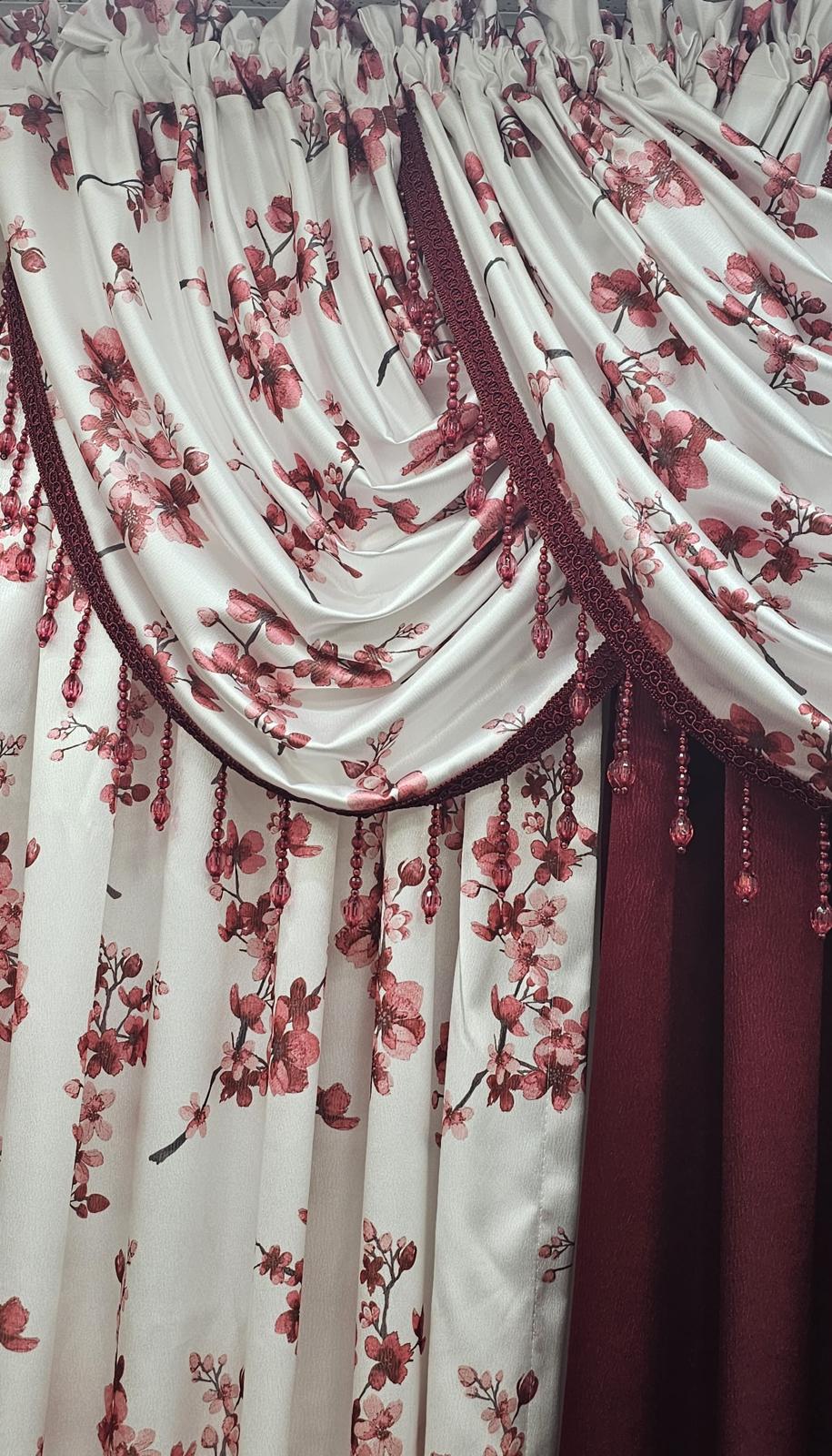A close-up of a decorative curtain panel with draped folds, featuring a white or warm off-white base printed with red and pink floral branches, plus a darker red inner curtain visible on the right.
