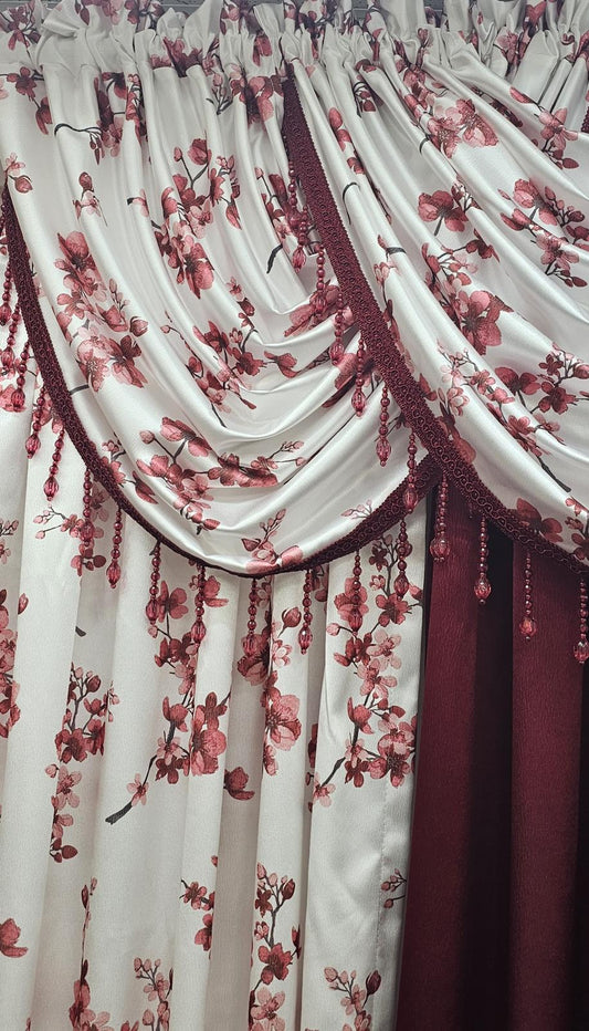 A close-up of a decorative curtain panel with draped folds, featuring a white or warm off-white base printed with red and pink floral branches, plus a darker red inner curtain visible on the right.