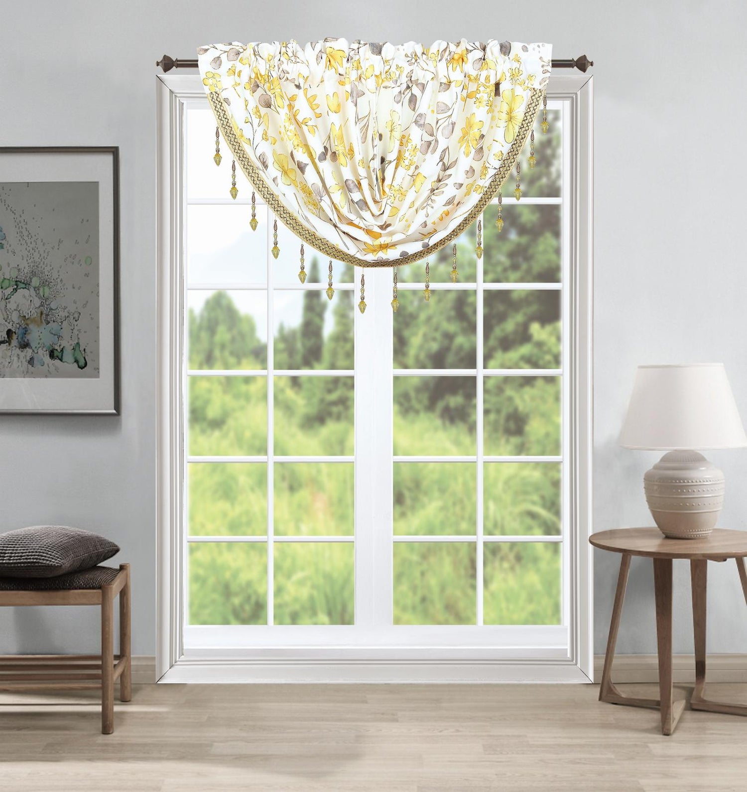 A sheer white window valance with a yellow and gray floral pattern and hanging gold-toned beads, styled in a bright room with a window showing green grass outside.