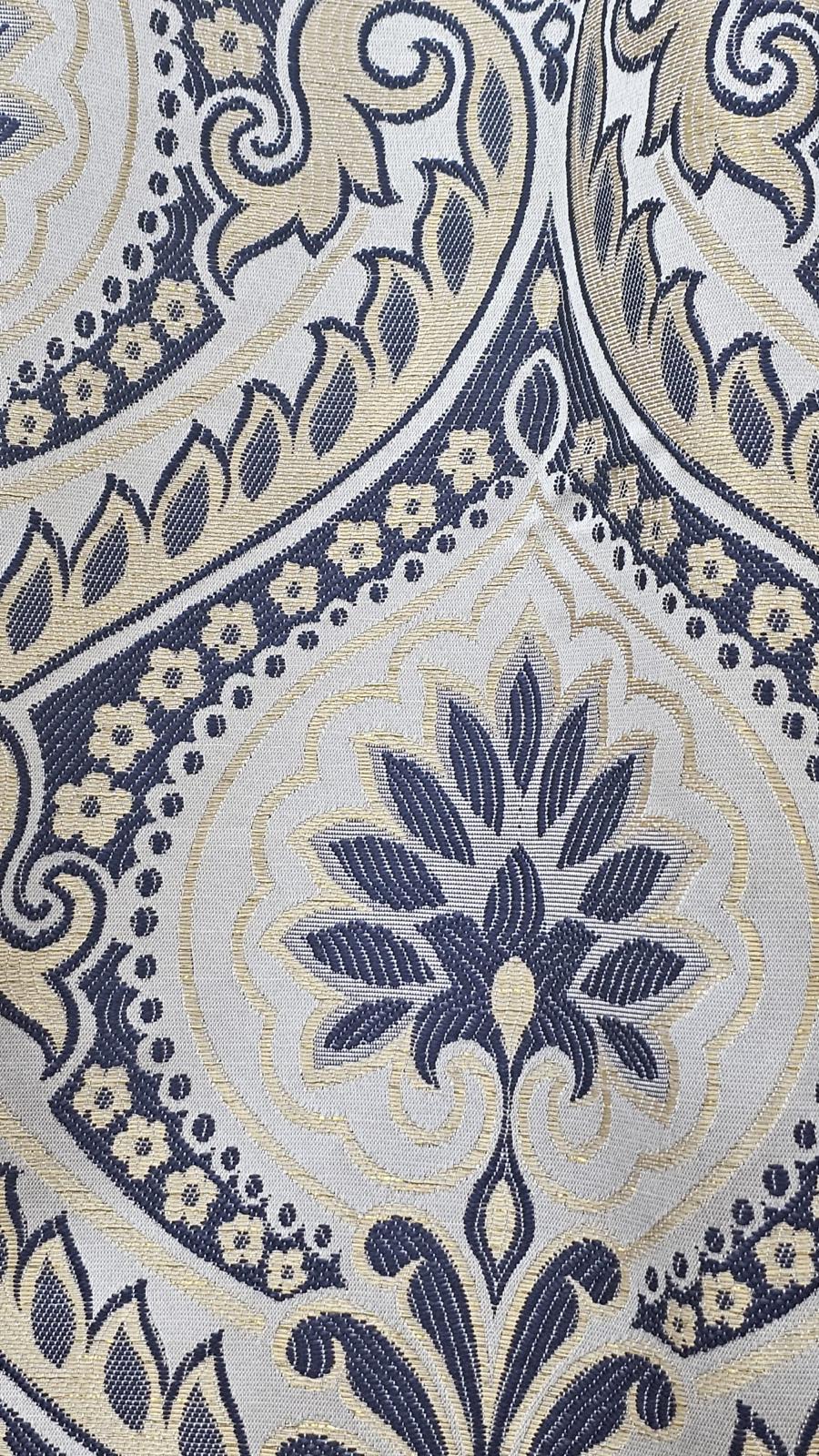 A close-up of an ornate woven fabric pattern with a central floral medallion and scrolling vine motifs in navy blue, beige, and white.