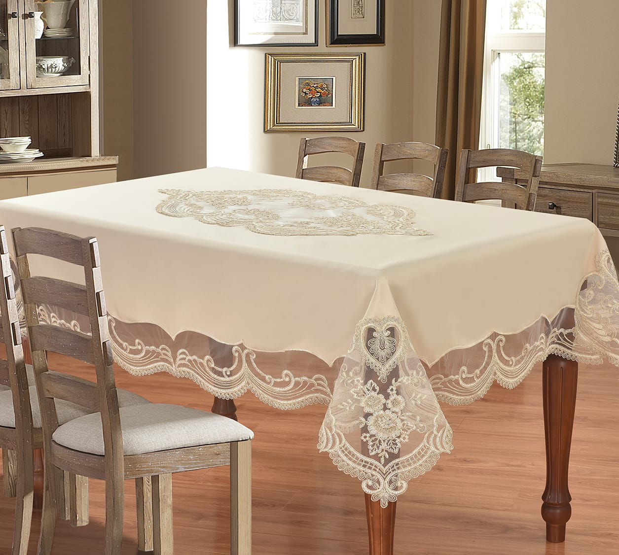An ivory tablecloth with a scalloped lace border and central embroidered motif, draped over a wooden dining table in a warm, decorated dining room.